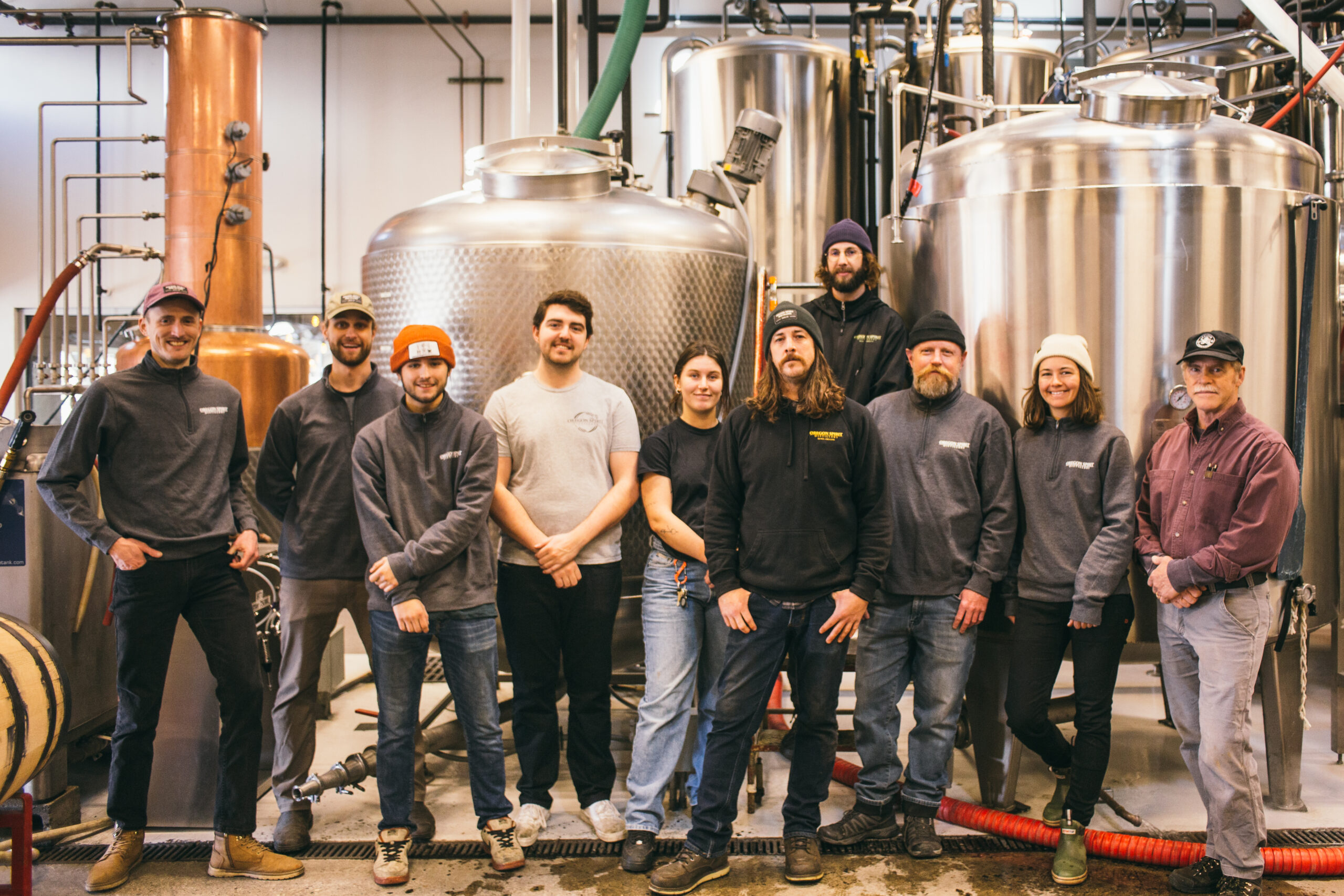 The Oregon Spirit Production team stands in front of the distillery equipment